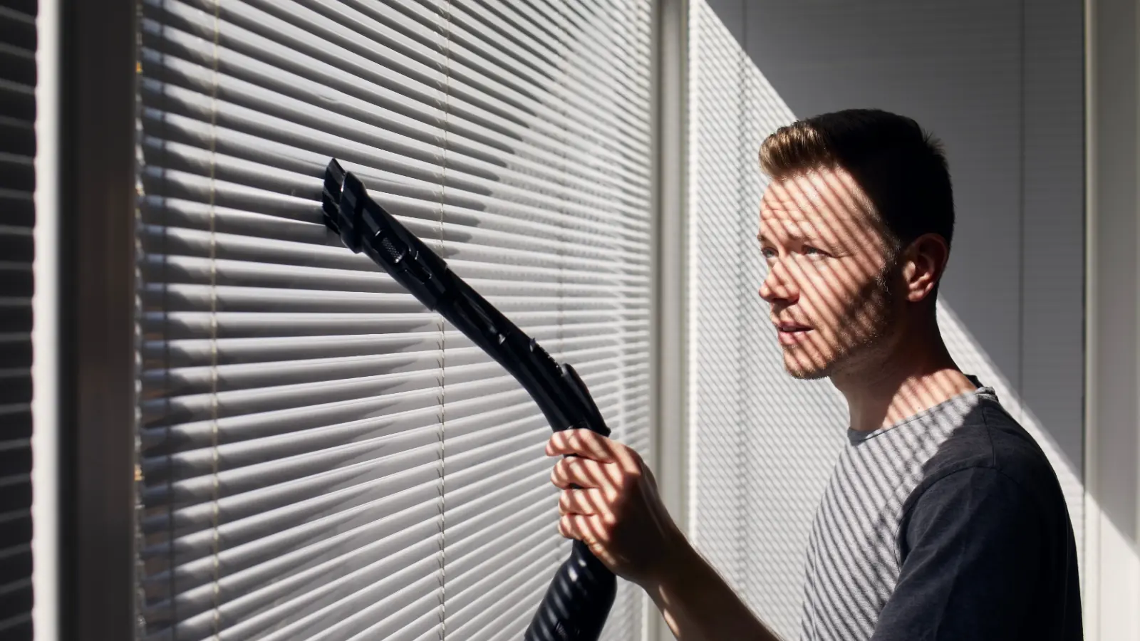 A man cleaning blinds with a vacuum cleaner