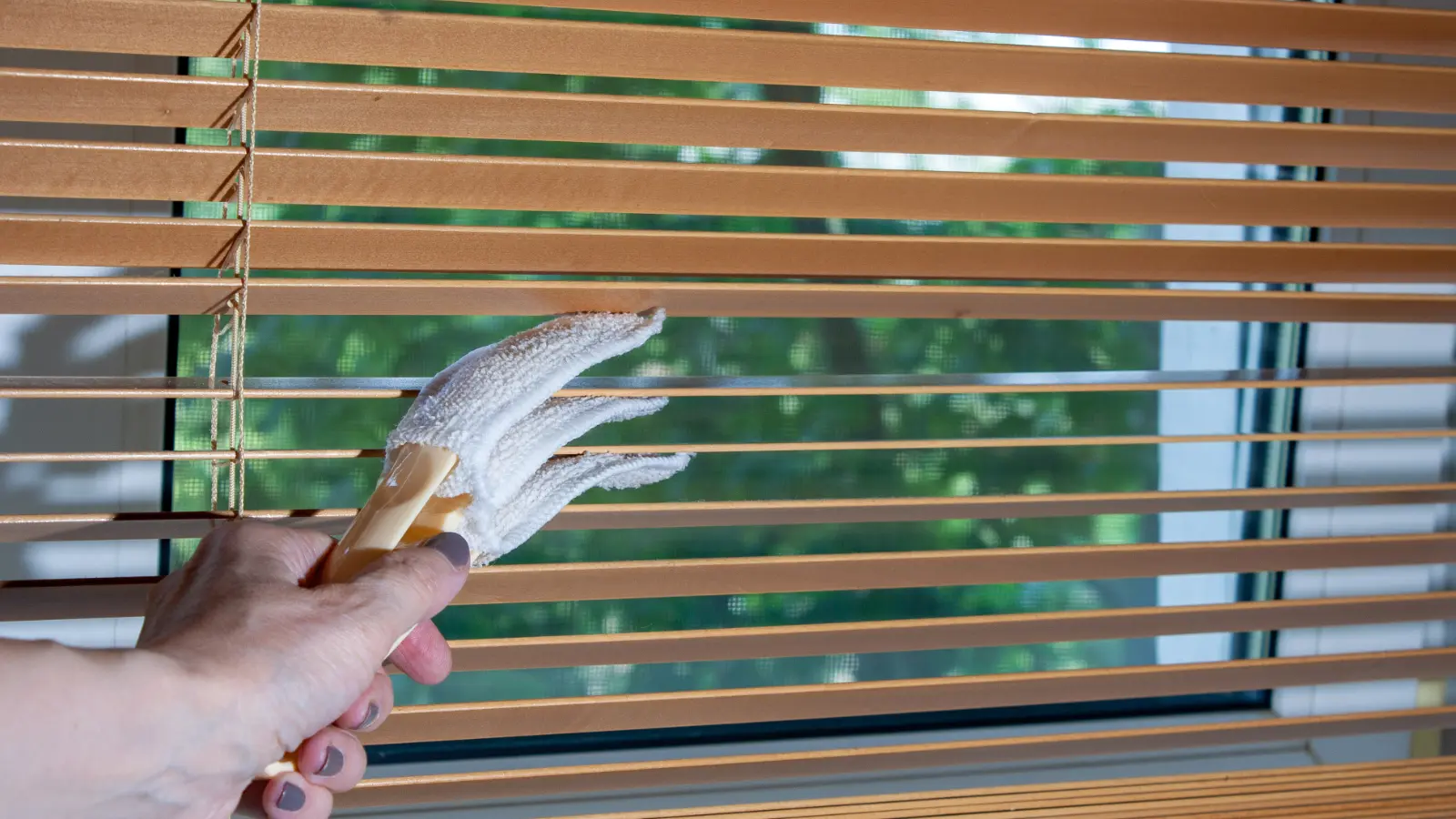 A woman cleaning wooden blinds with a brush