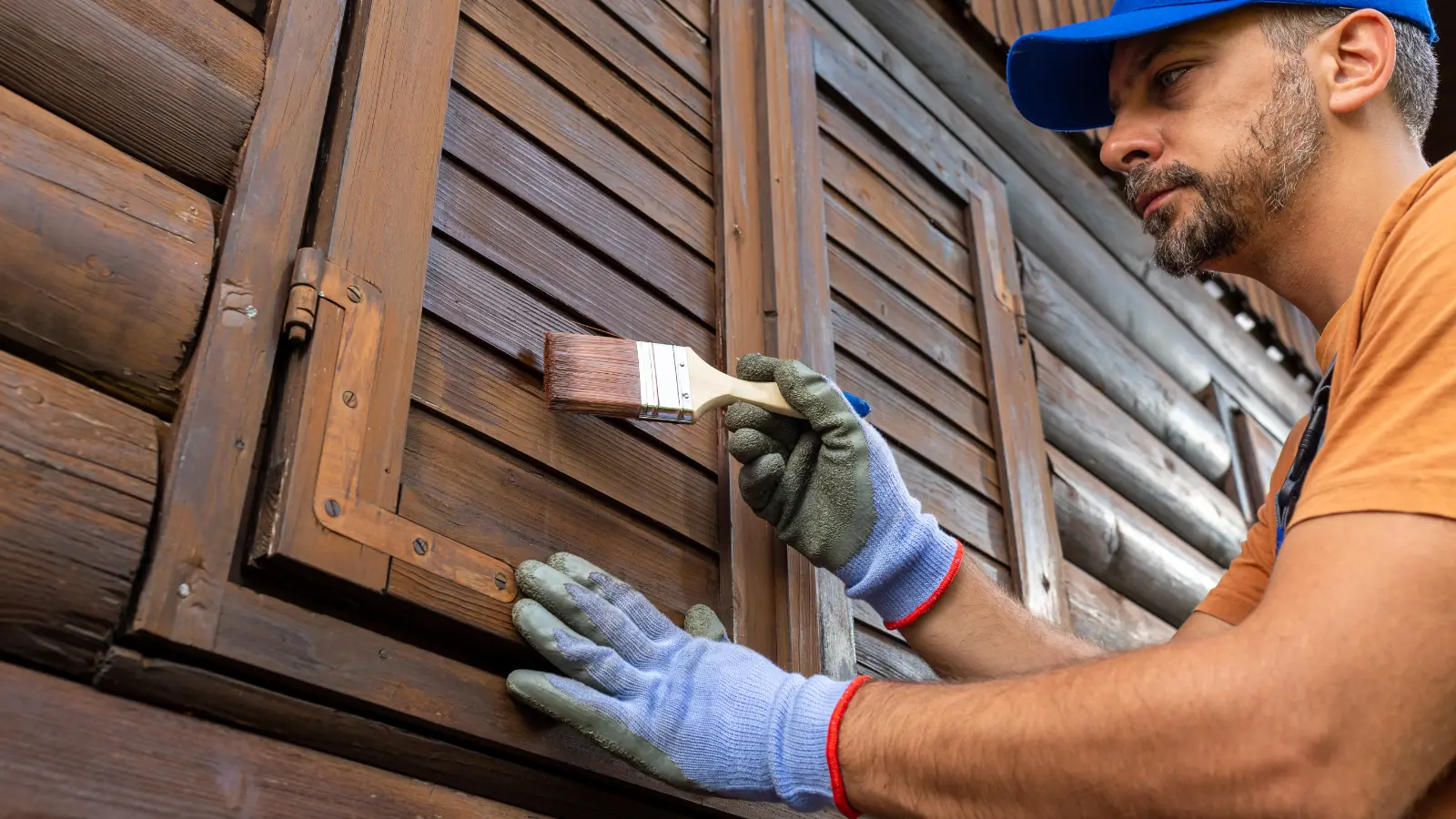 A man staining the shutters of a house.