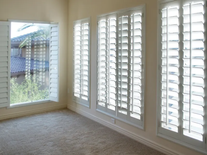 White plantation shutters in a room with large windows.
