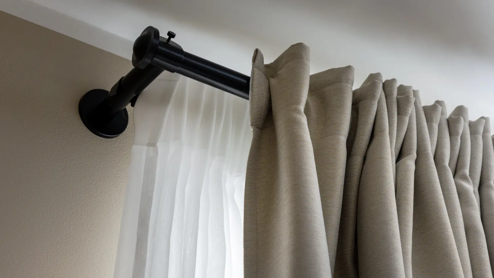 A black curtain rod with beige curtains